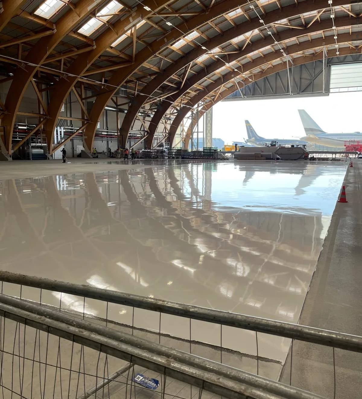 Hangar aéronautique neuf au sol en résine claire, charpente bois en arcs, avion au fond